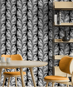 Black and white leaf wallpaper in dining room with pale wooden furniture and orange chairs