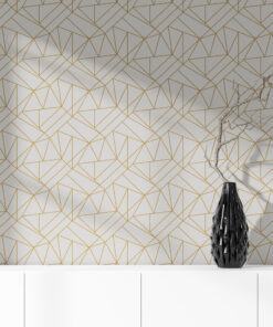 White and gold art deco geometric wallpaper on wall behind vase sitting on a white cabinet